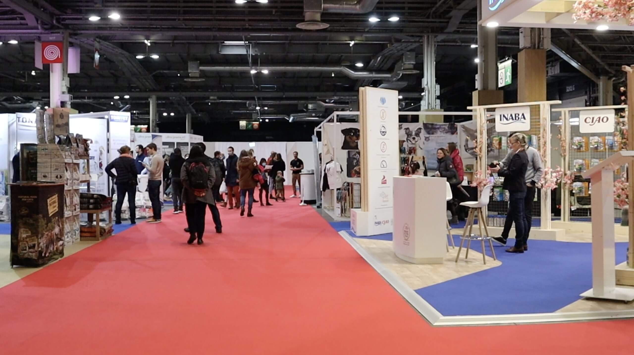 Visuel d'un couloir du salon Paris Animal Show, utilisateur de l'outil Planexpo. On y voit un gros stand sur la droite, ainsi que quelques visiteurs dans l'allée du salon, et des stands sur la gauche également.