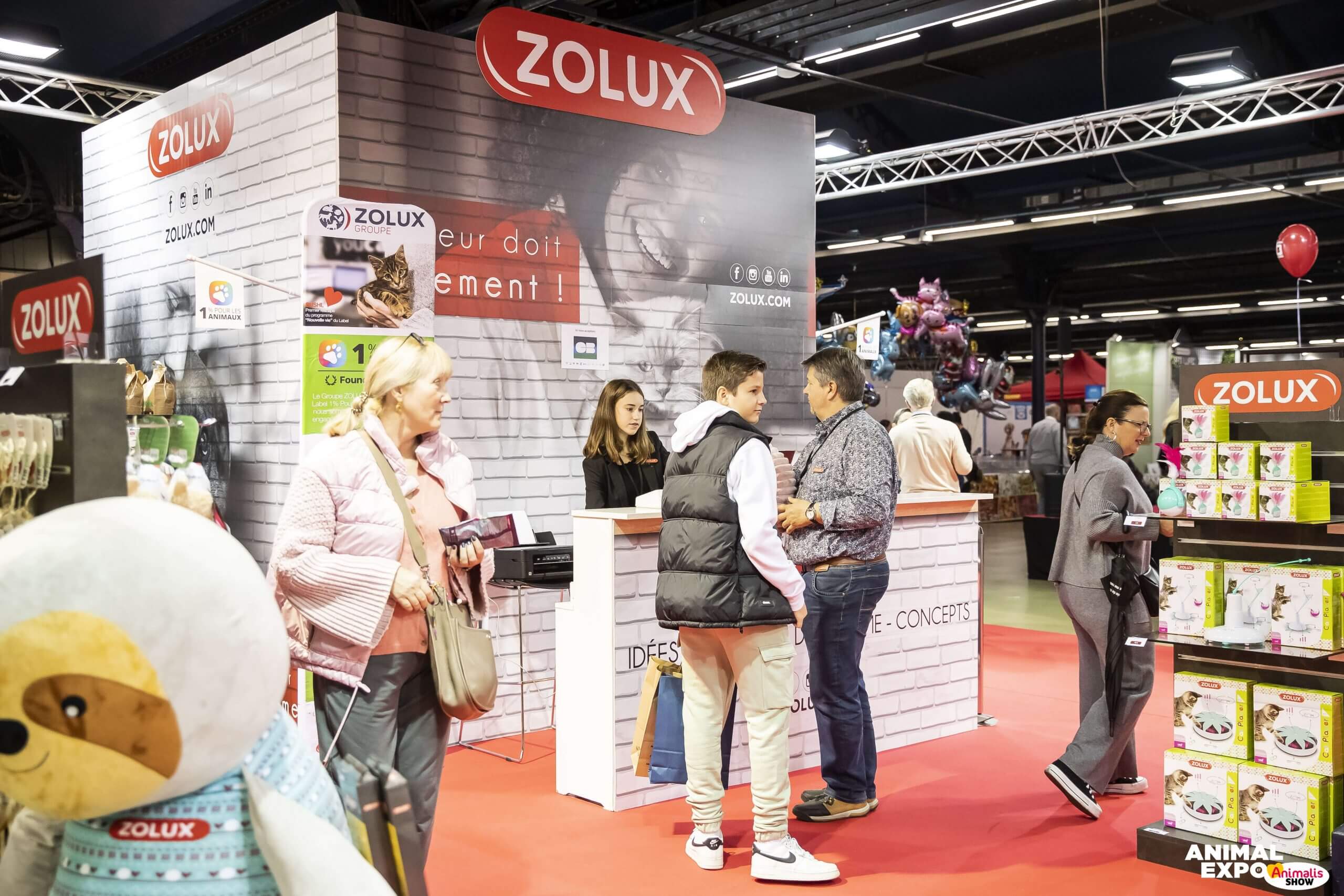 Photo d'un stand du salon Paris Animal Show d'Exposalons, utilisateur de l'outil de gestion événementielle Planexpo. On y voit 3 standistes et 2 visiteurs sur un stand de la marque Zolux. 