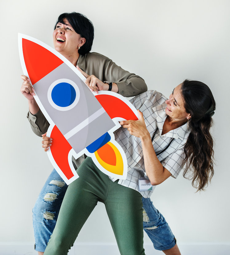 Photo de 2 femmes l'une derrière l'autre, qui tiennent une fusée dans les mains. Elles sont plutôt heureuse et regardent vers l'avenir. Le progrès et l'innovation sont moteurs de leur enthousiasme.
