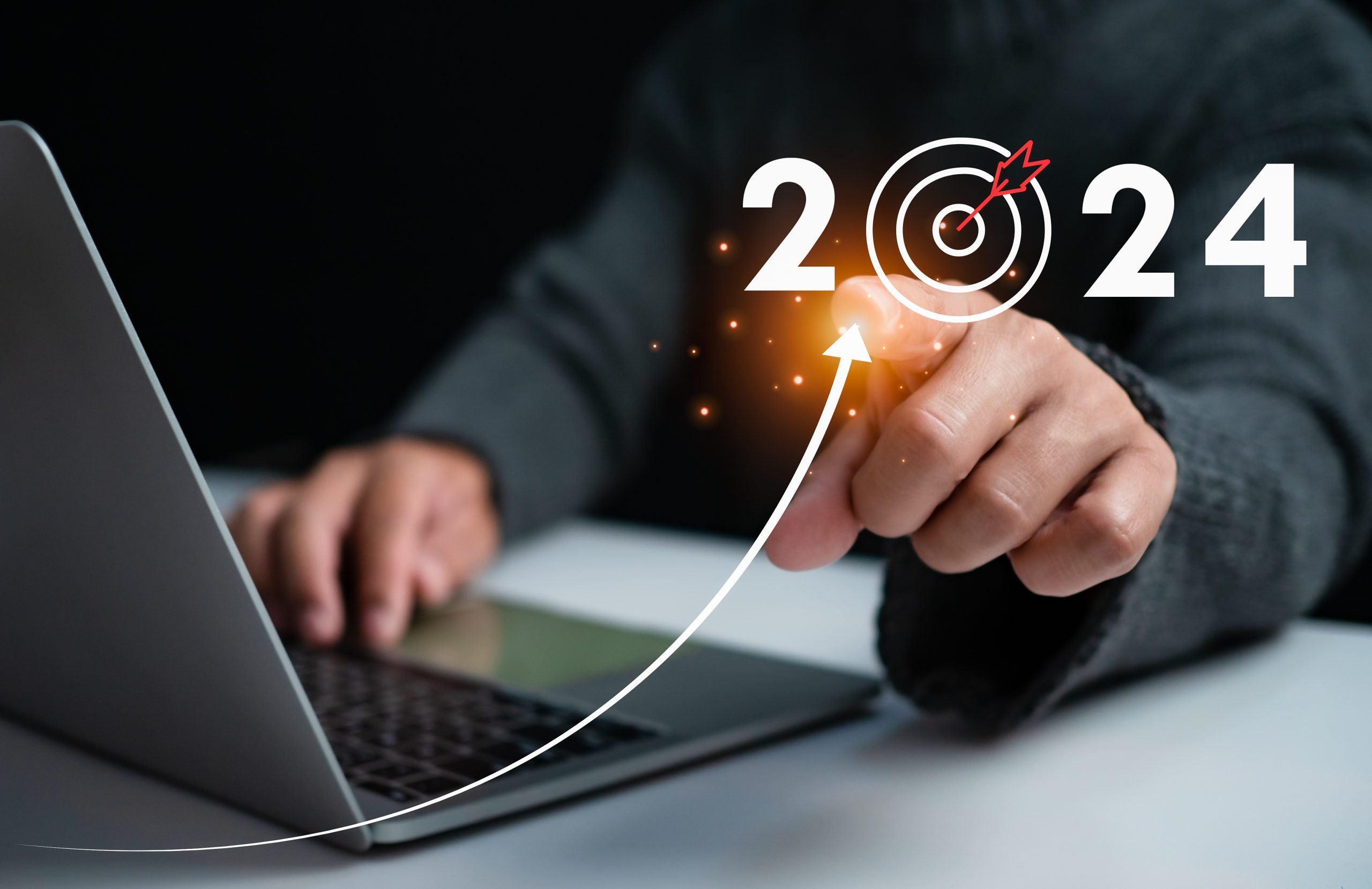 Image qui montre le buste d'un homme assis avec un pull, devant son ordinateur portable. Il pointe son doigt vers nous et fait apparaître l'année 2024 avec une flèche de croissance. Ça montre son ambition de développer son activité en 2024.