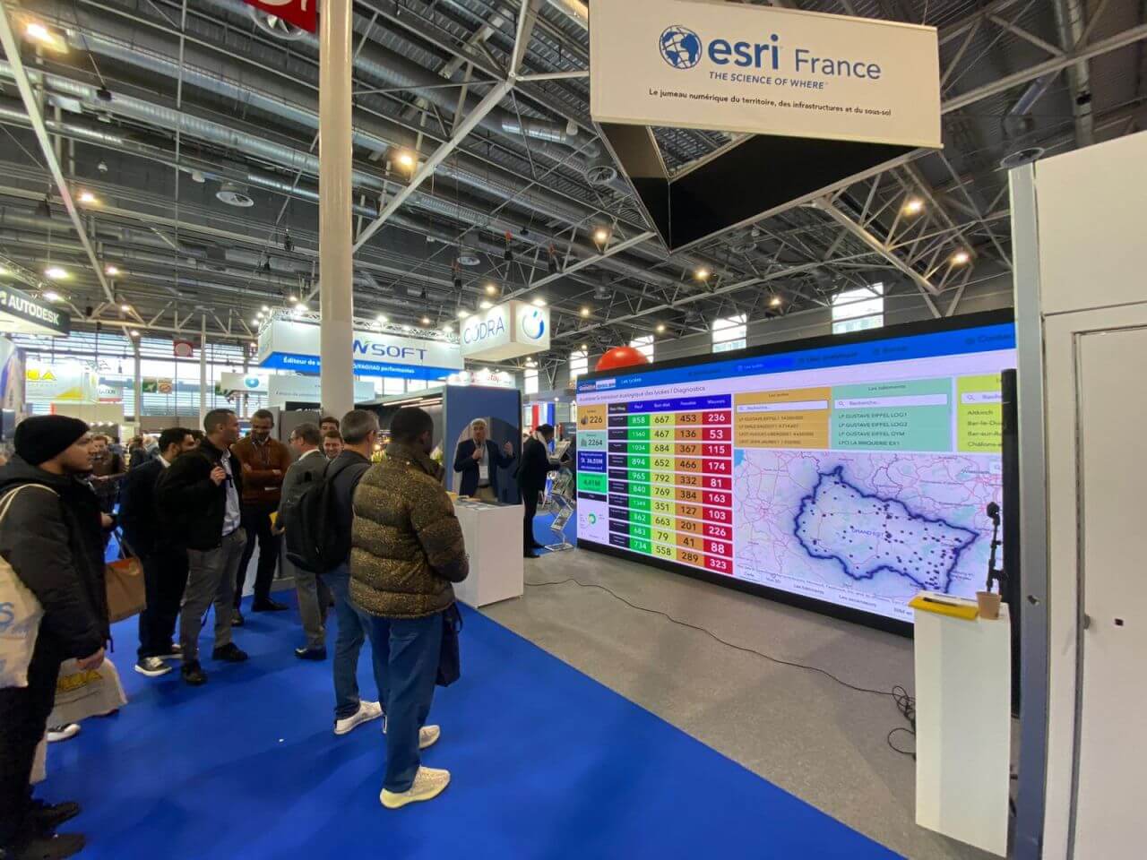 Photo d'un stand sur SIG - Esri France. On y voit une carte en fond de stand et un public placé juste devant.