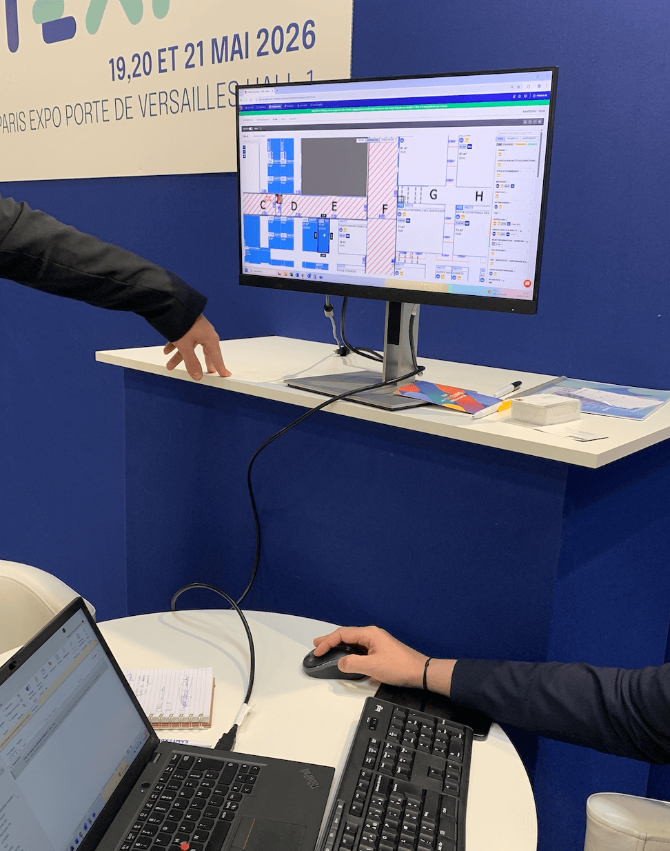 Vue plus détaillée du bureau commercial sur le stand du rebooking sur Santexpo. On y voit le plan commercial projeté sur un écran, ainsi que le commercial sur le côté droit.